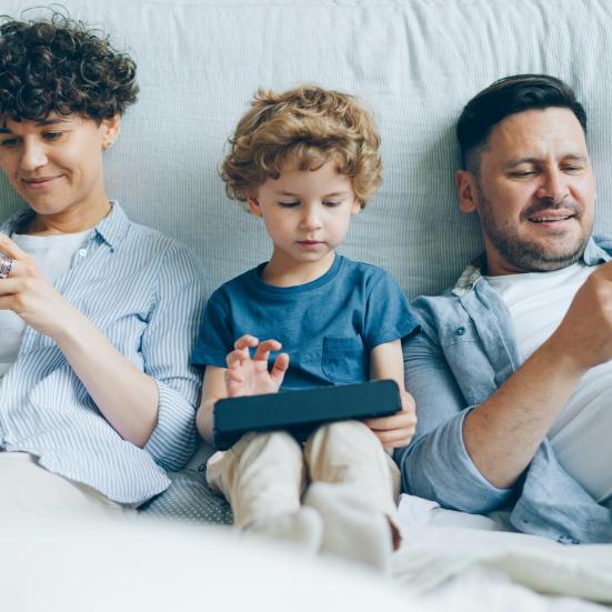 to børn og en mand sidder og kigger på hver sin telefon